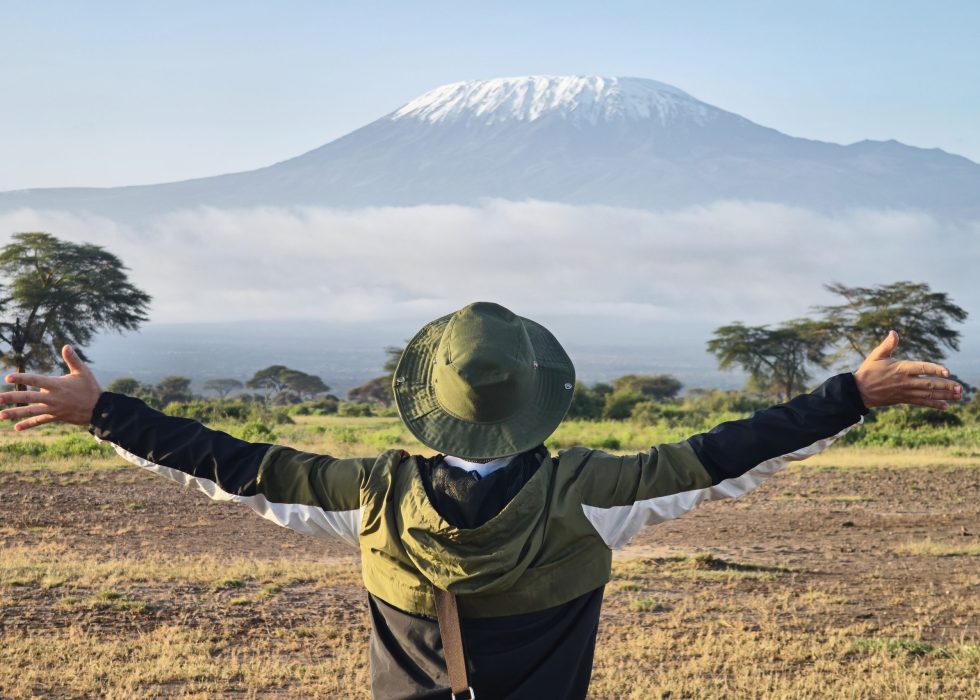 man walks against backdrop of Kilimanjaro. African walking safari. male traveler with backpack looking at amazing mountains. Hands to the side. travel concept, atmospheric epic moment